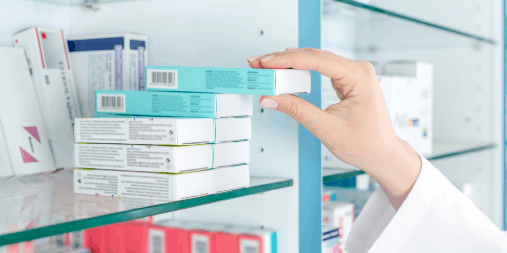 Préparateur en pharmacie qui saisit une boîte de médicament sur une étagère